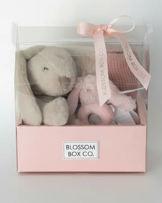 A baby hamper with a soft bunny and blanket in a clear box with pink ribbon