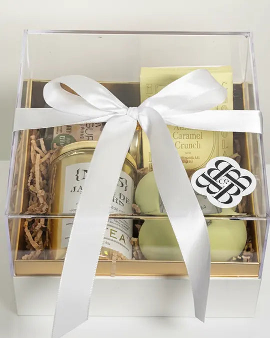 The BBCo Luxe Hamper under a clear lid, tied with white ribbon