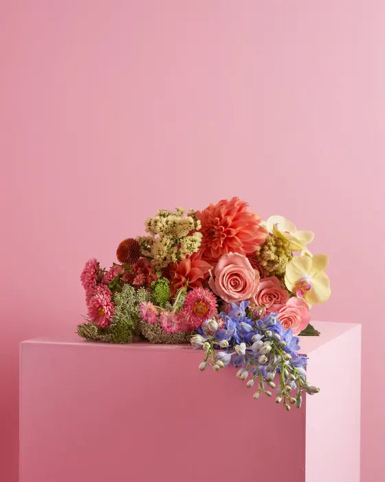A cascading arrangement of dahlias, roses and delphinium on a blush plinth