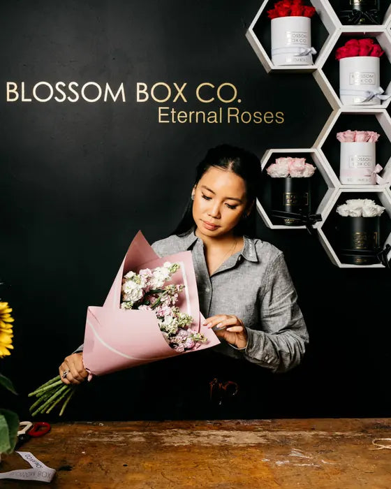 Trinh wrapping a bouquet of stock in pink paper in the studio