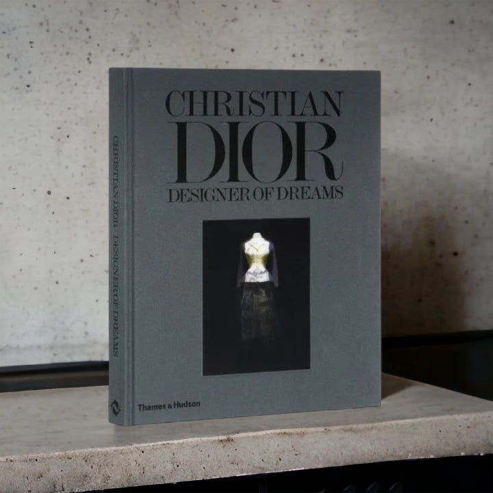 Christian Dior: Designer of Dreams hardcover book with a grey cover on a stone shelf