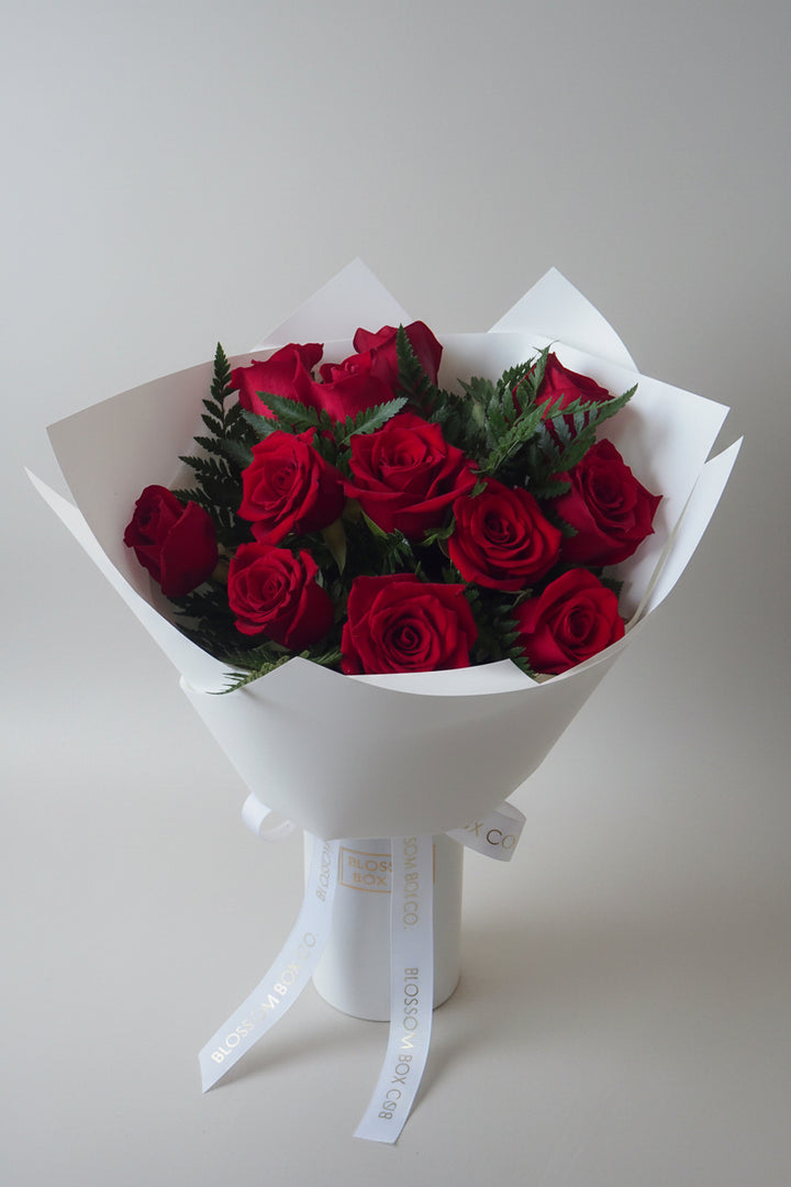 Deluxe Rose Bouquet of 12 red roses wrapped in white paper with a white ribbon