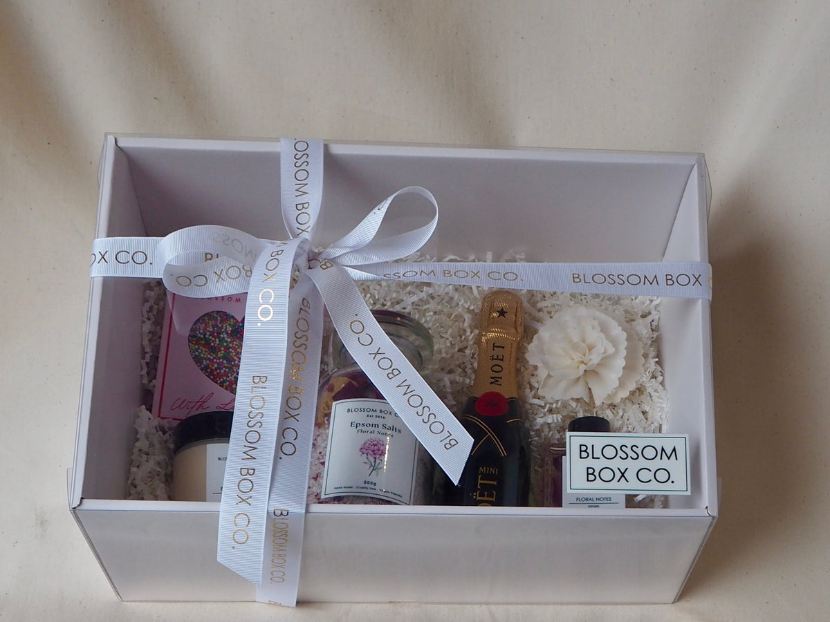 Indulge Hamper with mini champagne, chocolate, a candle and pamper gifts in a white gift box with ribbon